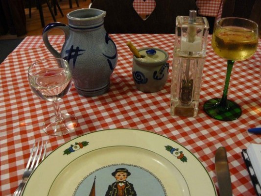 A table setting at a restaurant in Strasbourg, France: between the pitcher and the pepper grinder, a small, grey, ceramic pot is filled with Dijon mustard.