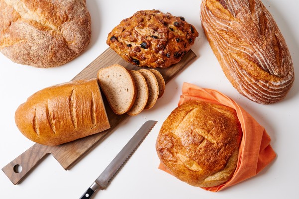 A selection of Zingerman's fresh baked bread loaves arranged on a cutting board with a bread knife.